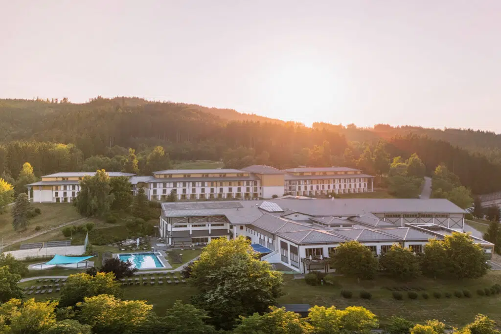 Luftaufnahme der Hotelanlage mit Pool und Wald im Abendlicht, Aldiana Club Ampflwang