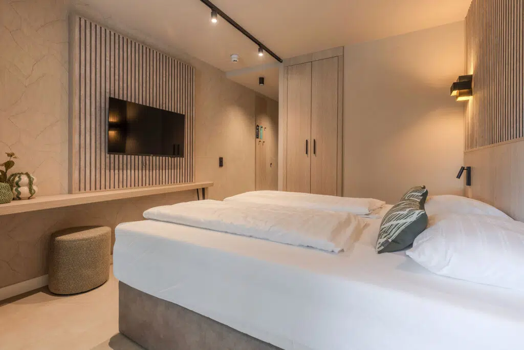Hotelzimmer mit Lattenwand aus Eiche, Wandbildschirm und geflochtenem Hocker, Aldiana Club Ampflwang