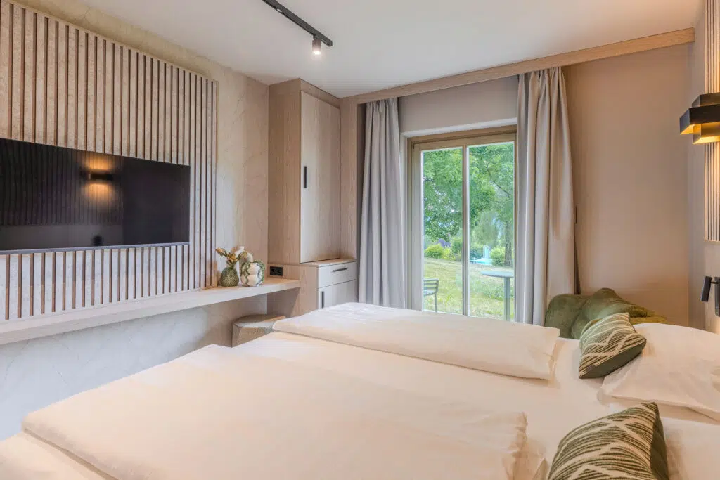 Zimmer mit grüner Sitzbank, bodentiefer Fensterfront und heller Holzkonsole, Aldiana Club Ampflwang