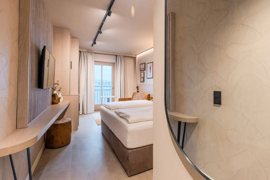 Blick am Rundspiegel vorbei auf Bett, TV-Wand und ockerfarbenen Sessel, Aldiana Club Ampflwang