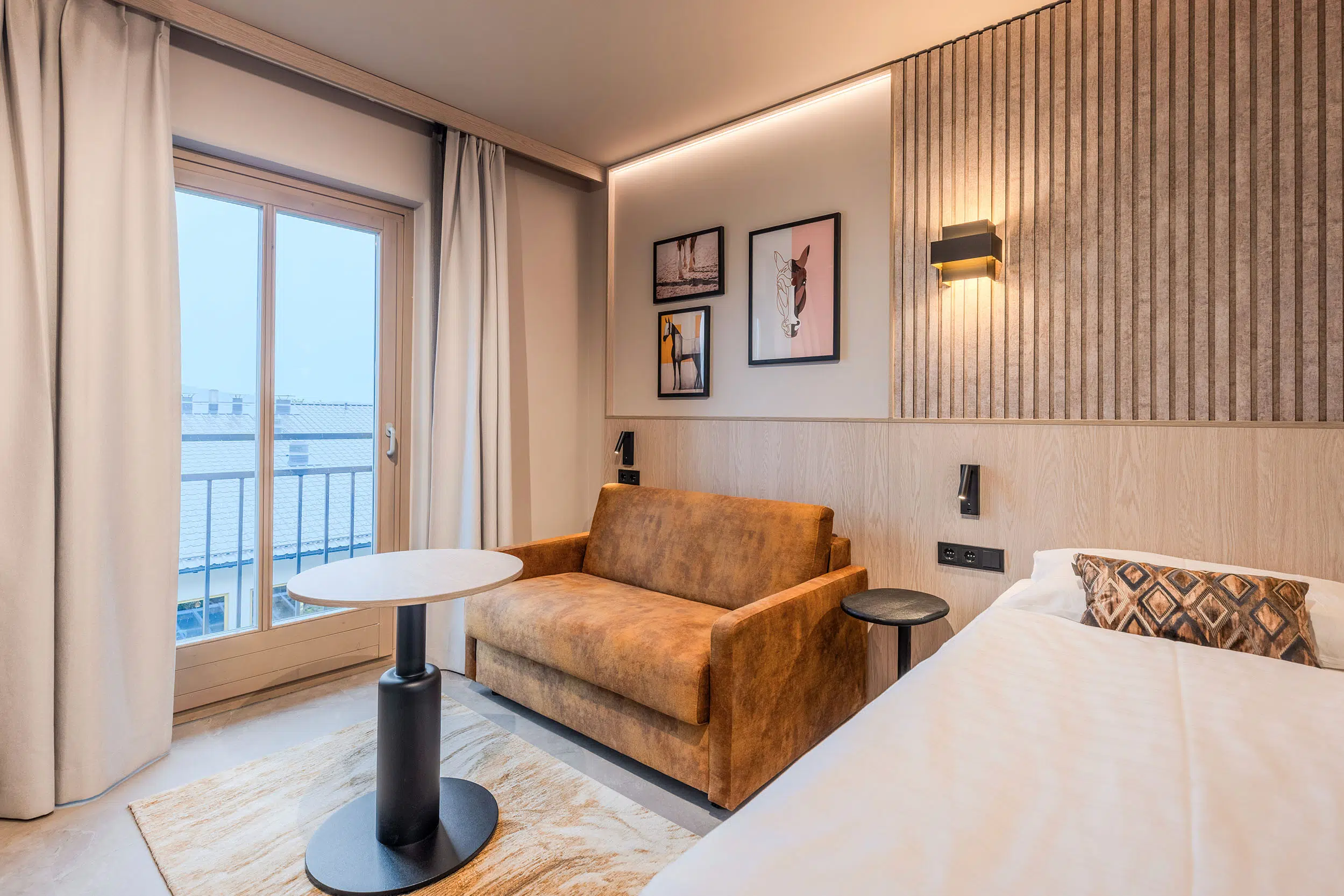 Hotelzimmer mit cognacfarbenem Sofa, Lamellenwand aus Holz und Pferdebildern, Aldiana Club Ampflwang