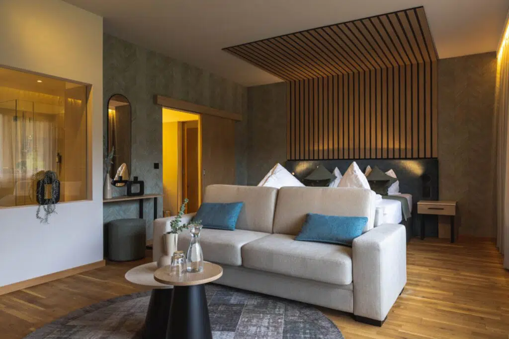 Wohn- und Schlafbereich mit beigem Sofa, blauen Kissen und Fischgrätwand, Aldiana Club Salzkammergut