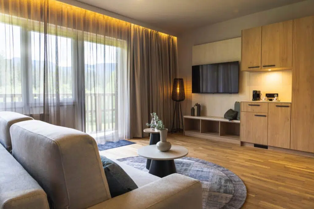 Wohnbereich mit grauem Sofa, TV-Wand und Küchenzeile aus Eiche, Aldiana Club Salzkammergut
