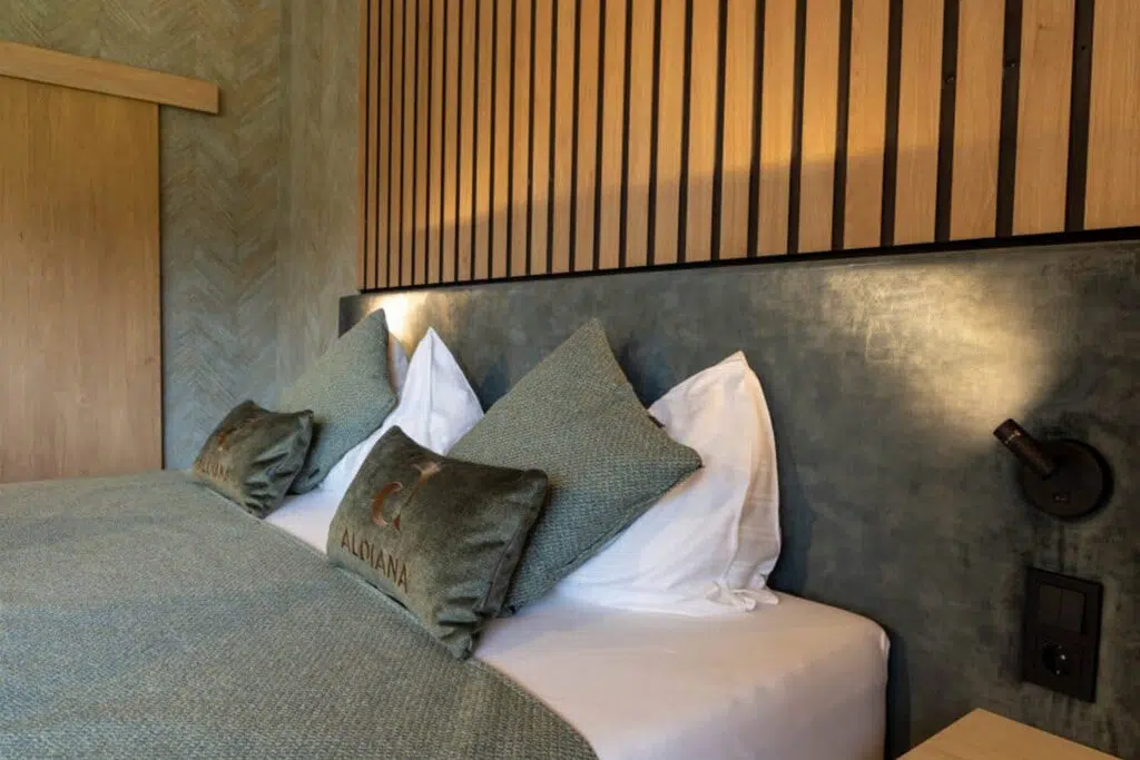 Bettkopfteil in Betonoptik mit Eichenlamellen, grünen Kissen und schwarzer Leseleuchte, Aldiana Club Salzkammergut