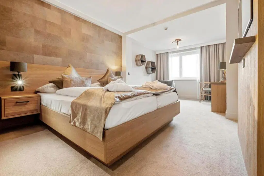Geräumiges Zimmer mit Holzpaneelwand, goldfarbener Tagesdecke und Wabenregalen, Aldiana Club Schlanitzen Alm