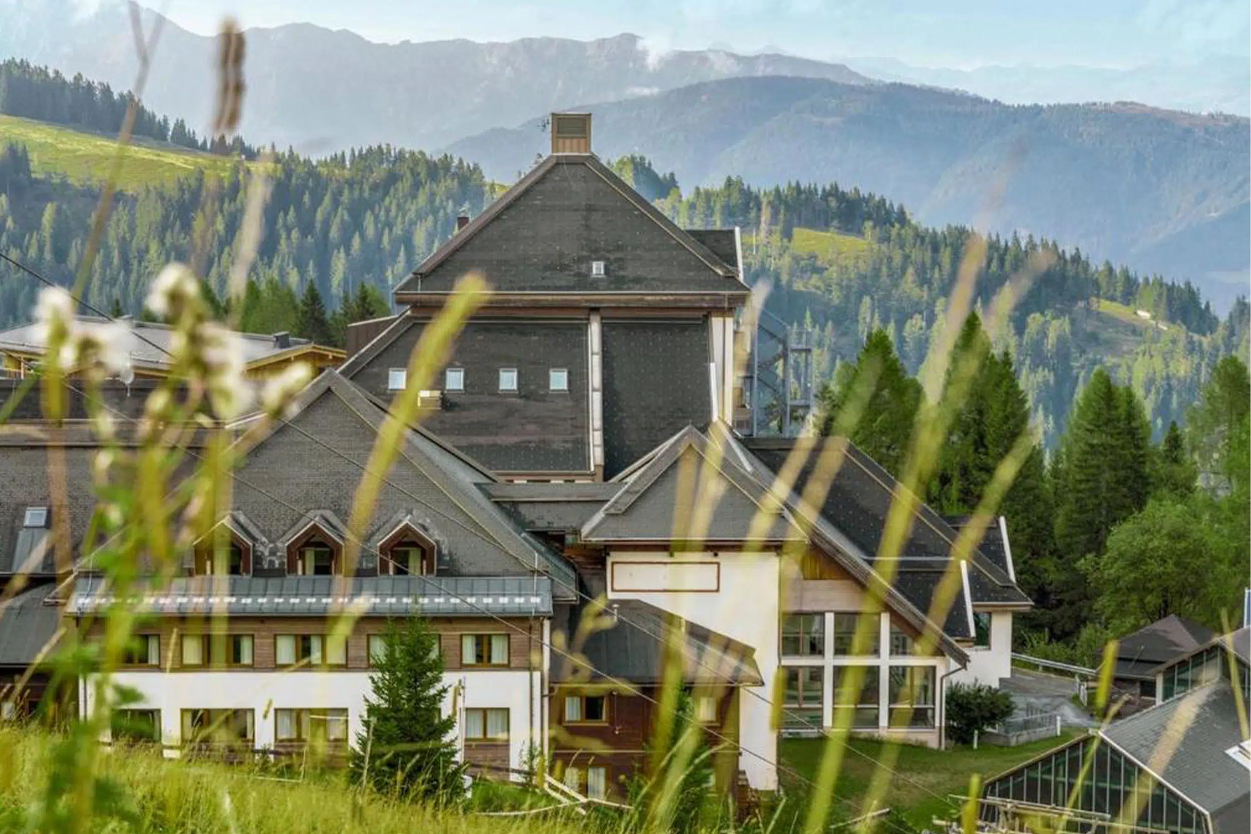 Hotelgebäude mit dunklen Giebeldächern vor bewaldeten Bergen, Aldiana Club Schlanitzen Alm