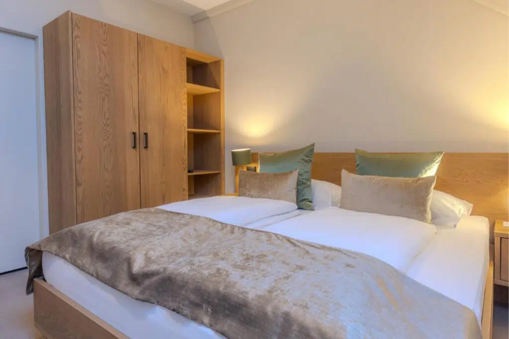 Schlafzimmer mit Eichenschrank, offenem Regal und Doppelbett mit grünen Kissen, Aldiana Club Schlanitzen Alm