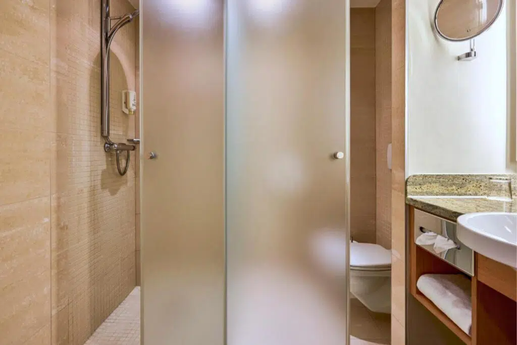 Hotelbadezimmer mit beigen Natursteinfliesen, Dusche hinter Milchglas und Granitwaschtisch, Aldiana Club Schlanitzen Alm
