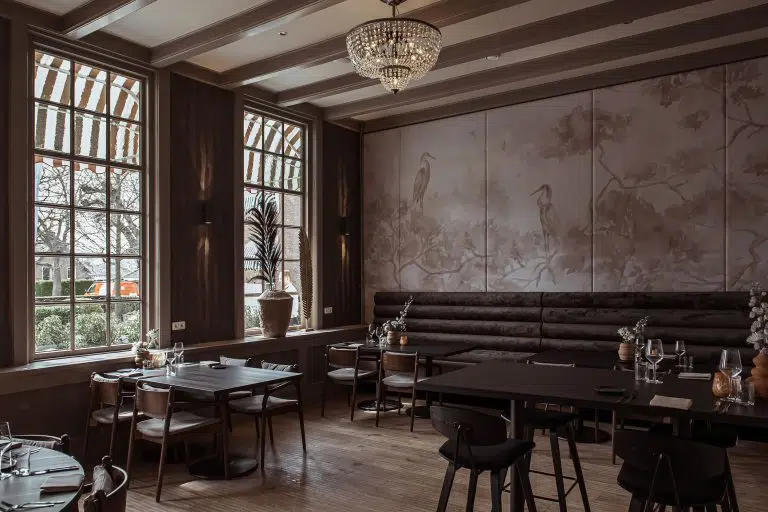 Restaurant mit Kronleuchter, Wandbild mit Reihern und dunkler Polsterbank an Holztischen