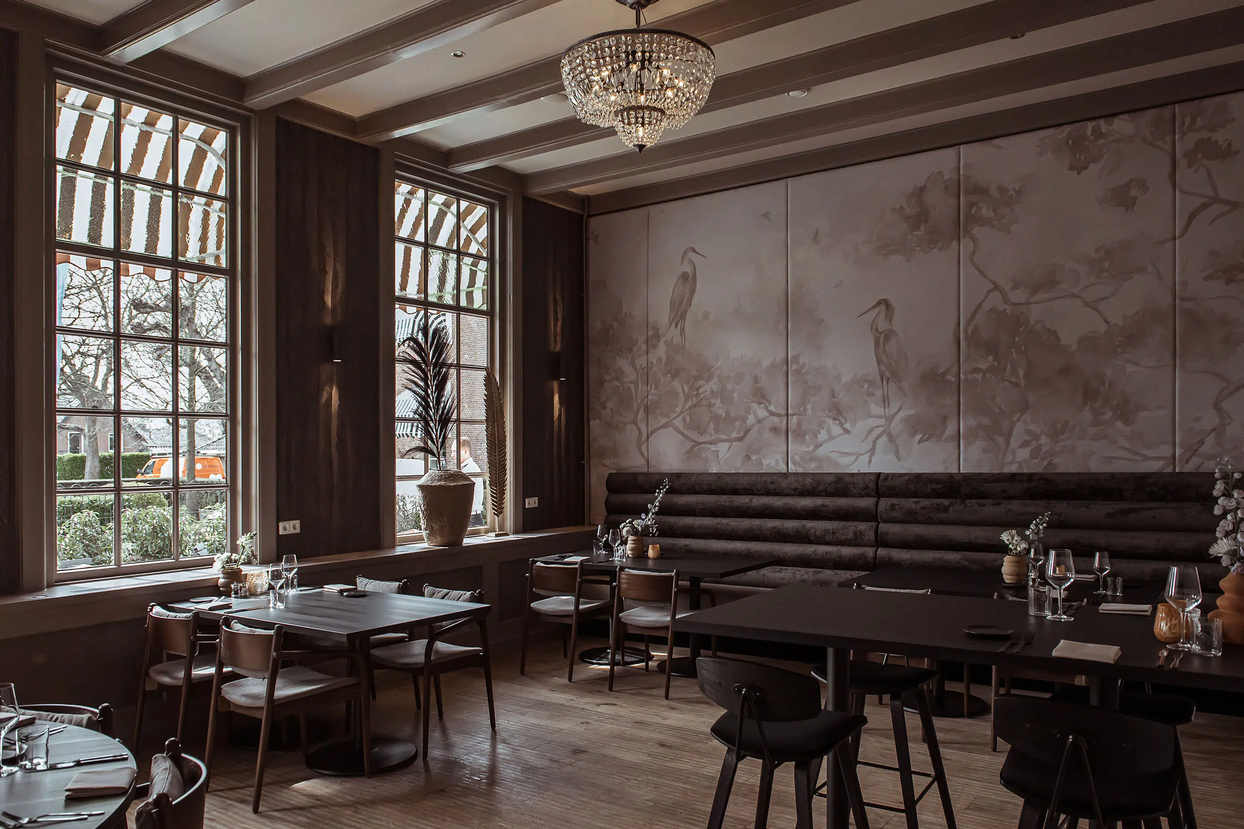 Restaurant mit Kronleuchter, Wandbild mit Reihern und dunkler Polsterbank an Holztischen