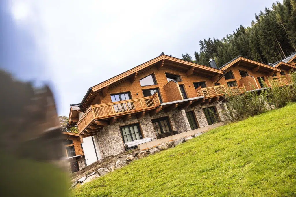 Chalet mit Holzbalkon und Natursteinfassade auf einem Wiesenhang, Tauernlodge