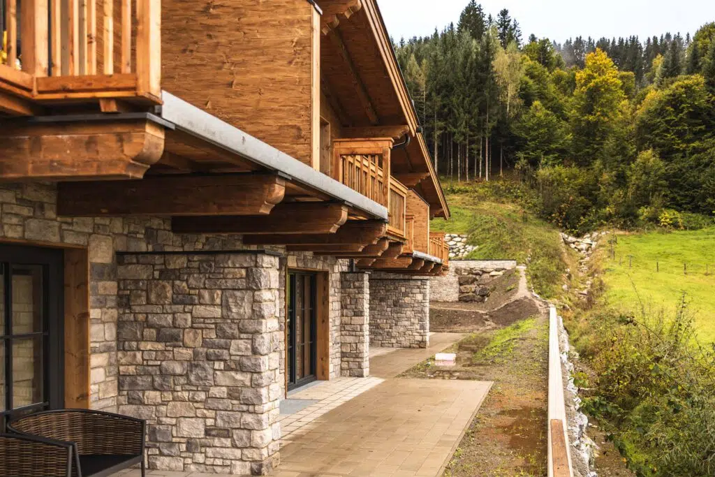 Terrasse mit Steinpfeilern und Holzbalkonen entlang der Chalets, Tauernlodge