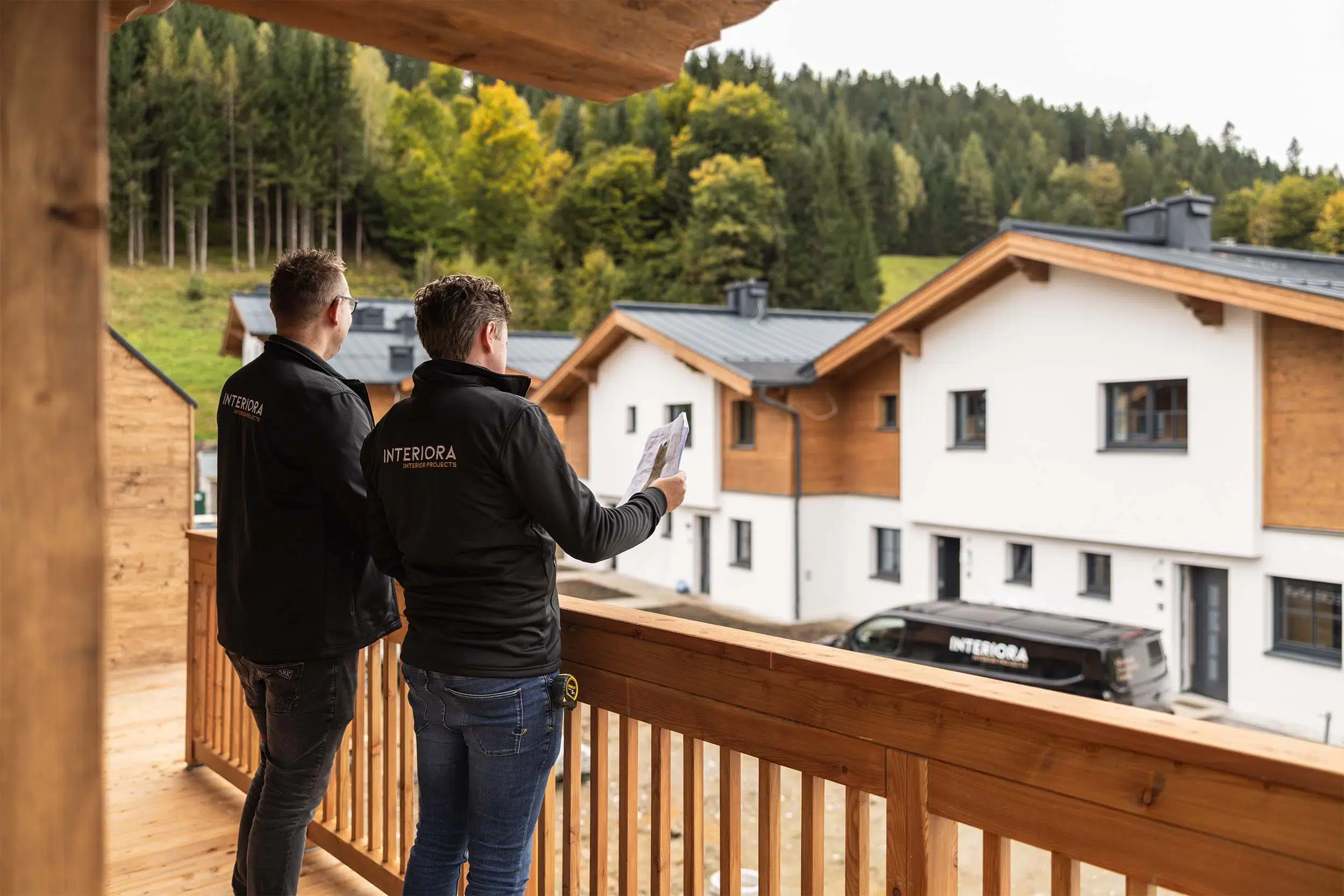 Zwei Mitarbeitende von Interiora auf einem Holzbalkon mit Blick auf neue Chalets