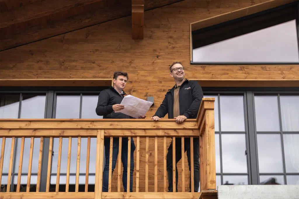 Zwei Männer mit Bauplan auf dem Balkon eines Chalets, Tauernlodge