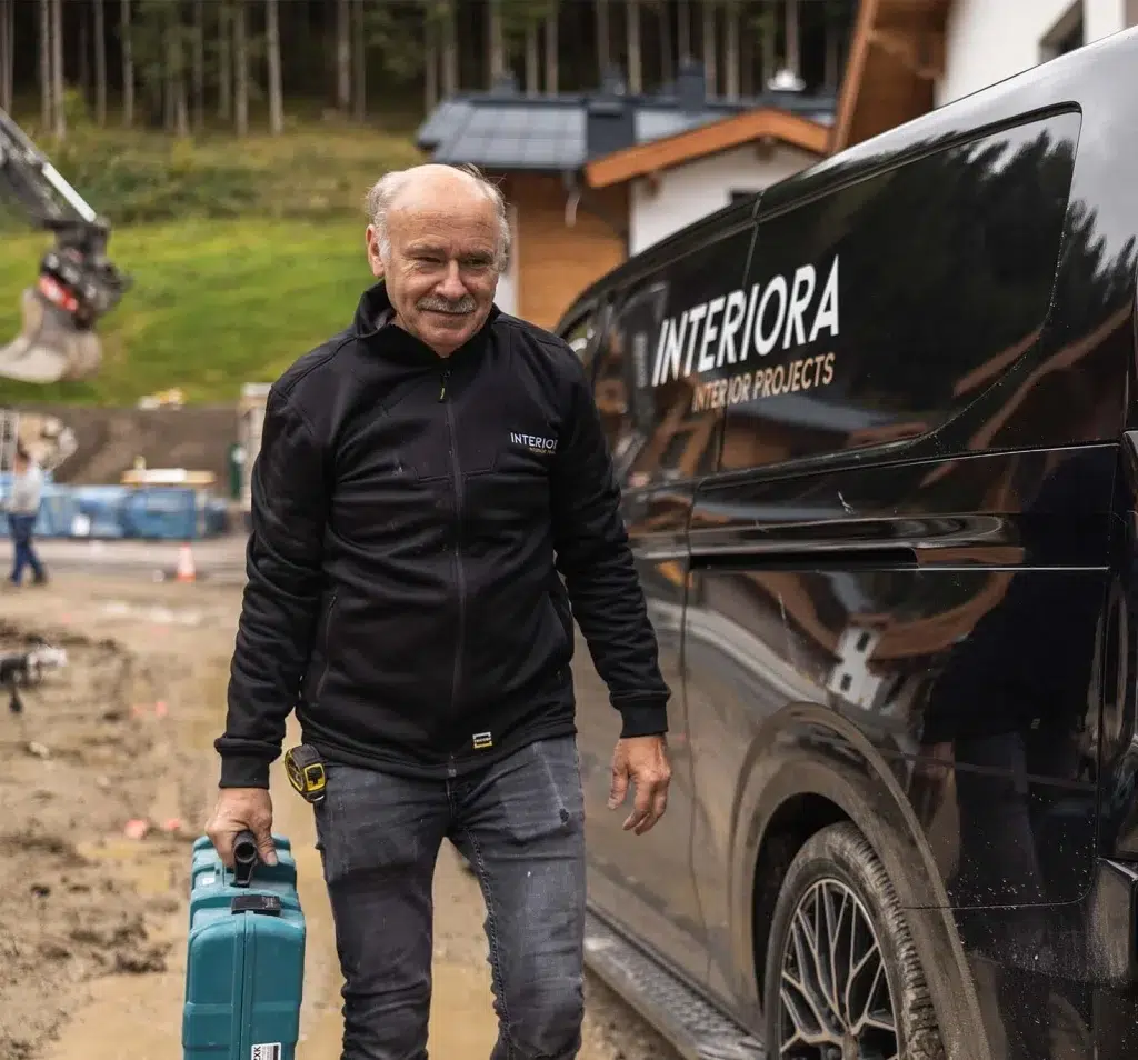 Monteur mit Werkzeugkoffer neben dem schwarzen Firmenbus auf der Baustelle