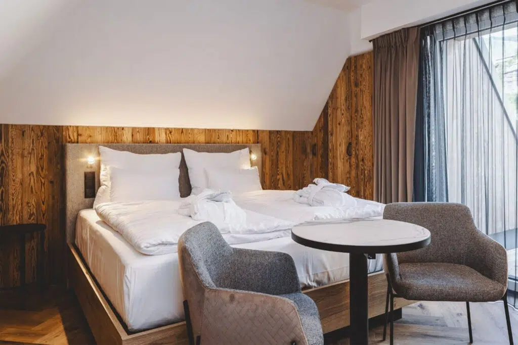 Hotelzimmer mit Altholzwand, gepolstertem Kopfteil und Marmortisch mit zwei Sesseln, The Gast House