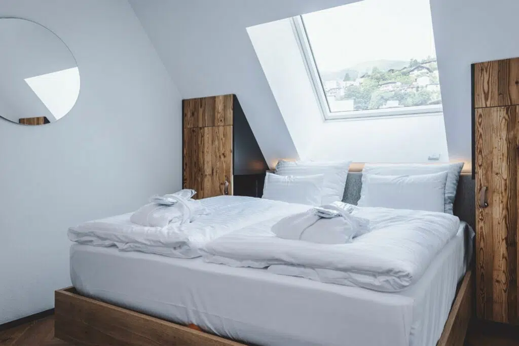 Dachzimmer mit Doppelbett, rundem Spiegel und Altholzschränken unter der Dachschräge, The Gast House