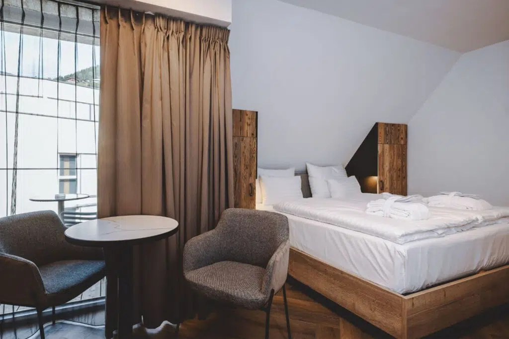 Hotelzimmer mit Altholzschränken, grauen Sesseln und Marmortisch am Fenster, The Gast House