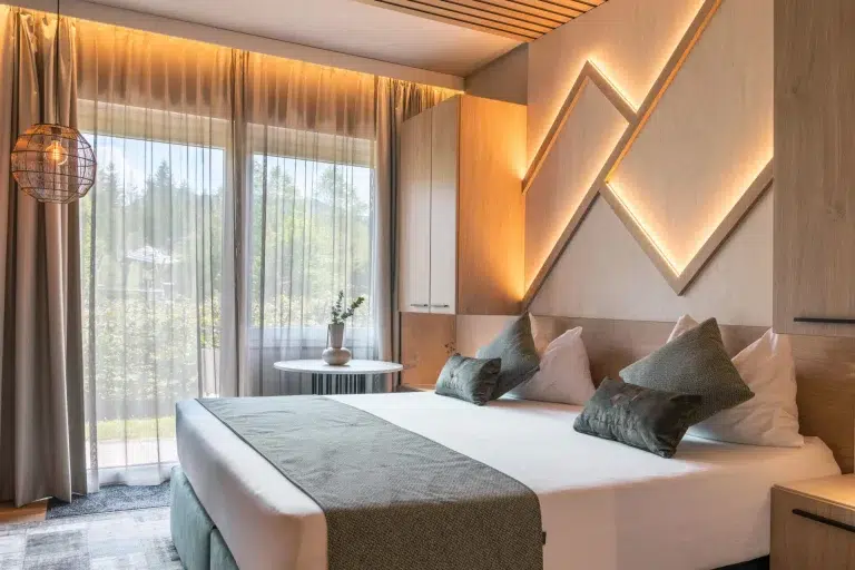 Hotelzimmer mit Holzwand, indirekt beleuchtetem Bergmotiv und grauen Kissen auf dem Doppelbett