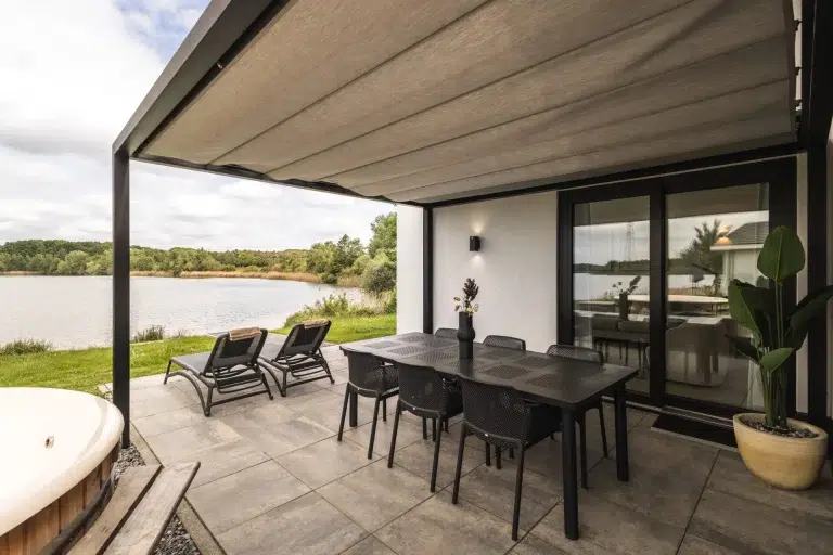 Überdachte Terrasse mit schwarzen Gartenmöbeln, Holzbadezuber und Blick auf den See